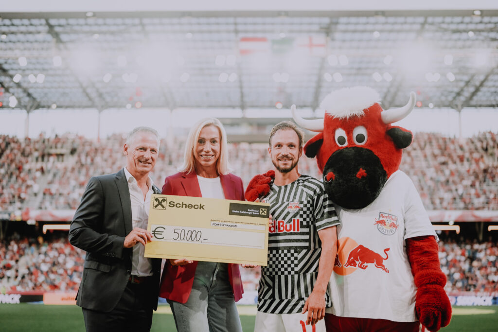 Anita Gerhardter mit Bank-Scheck vor Publikum in einem Fußballstadion