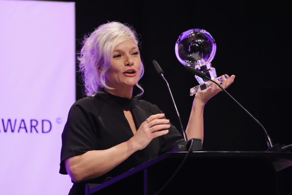 Ina Müller hält Preis in der Hand und steht vor Rednerpult
