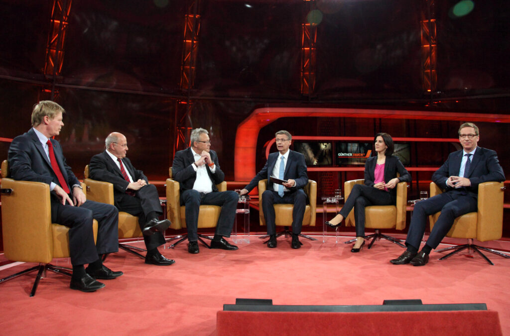 Michael Hüther sitzt mit fünf anderen Gästen bei einer Podiumsdiskussion