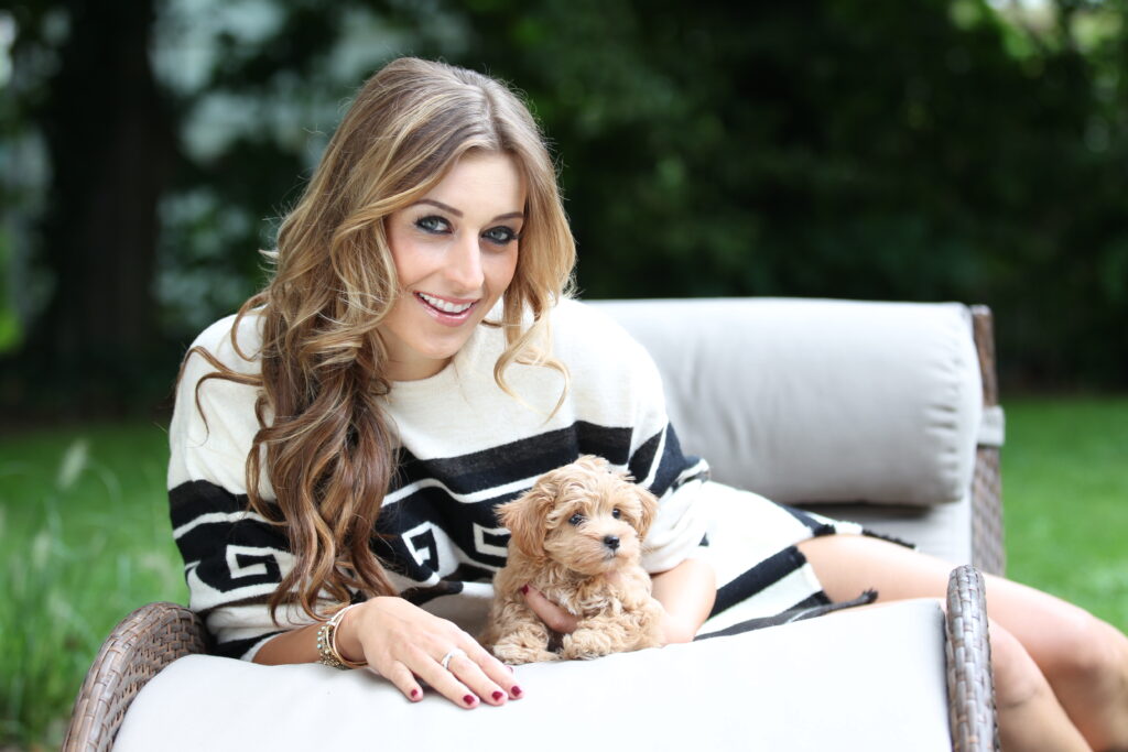 Verena Kerth mit Hund Verena Kerth sitzt mit einem kleinen Hund in der Hand auf einem Gartensofa und lächelt in die Kamera