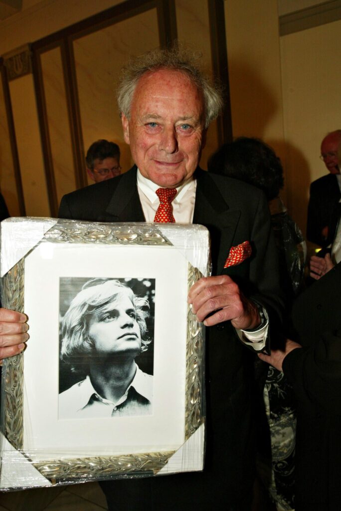Reinhold Würth Reinhold Würth hält ein Bild mit silbernen Rahmen und einem jungen Mann in seinen Händen und lacht in die Kamera