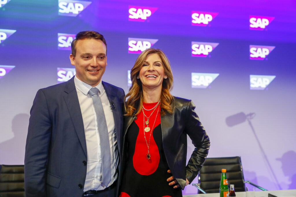 Christian Klein steht mit Anzug gekleidet neben einer Dame auf einer Bühne. Dahinter ist das SAP Logo mehrmals sichtbar