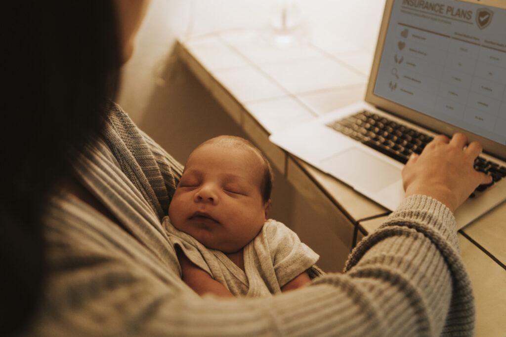 Gülcan Kamps Frau die ein Baby in der Hand hält und vor einem PC sitzt und etwas schreibt