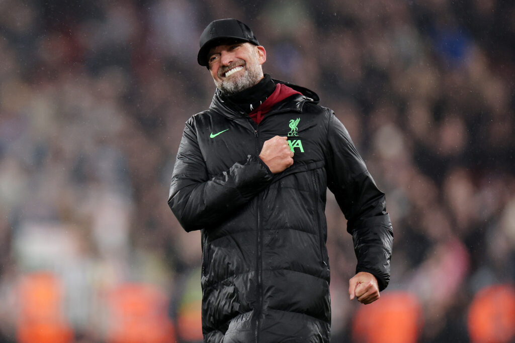 Jürgen Klopp Jürgen Klopp trägt einen schwarzen sportlichen Mantel und eine schwarze Kappe. Er legt eine Hand auf sein Herz und lächelt sehr entspannt.