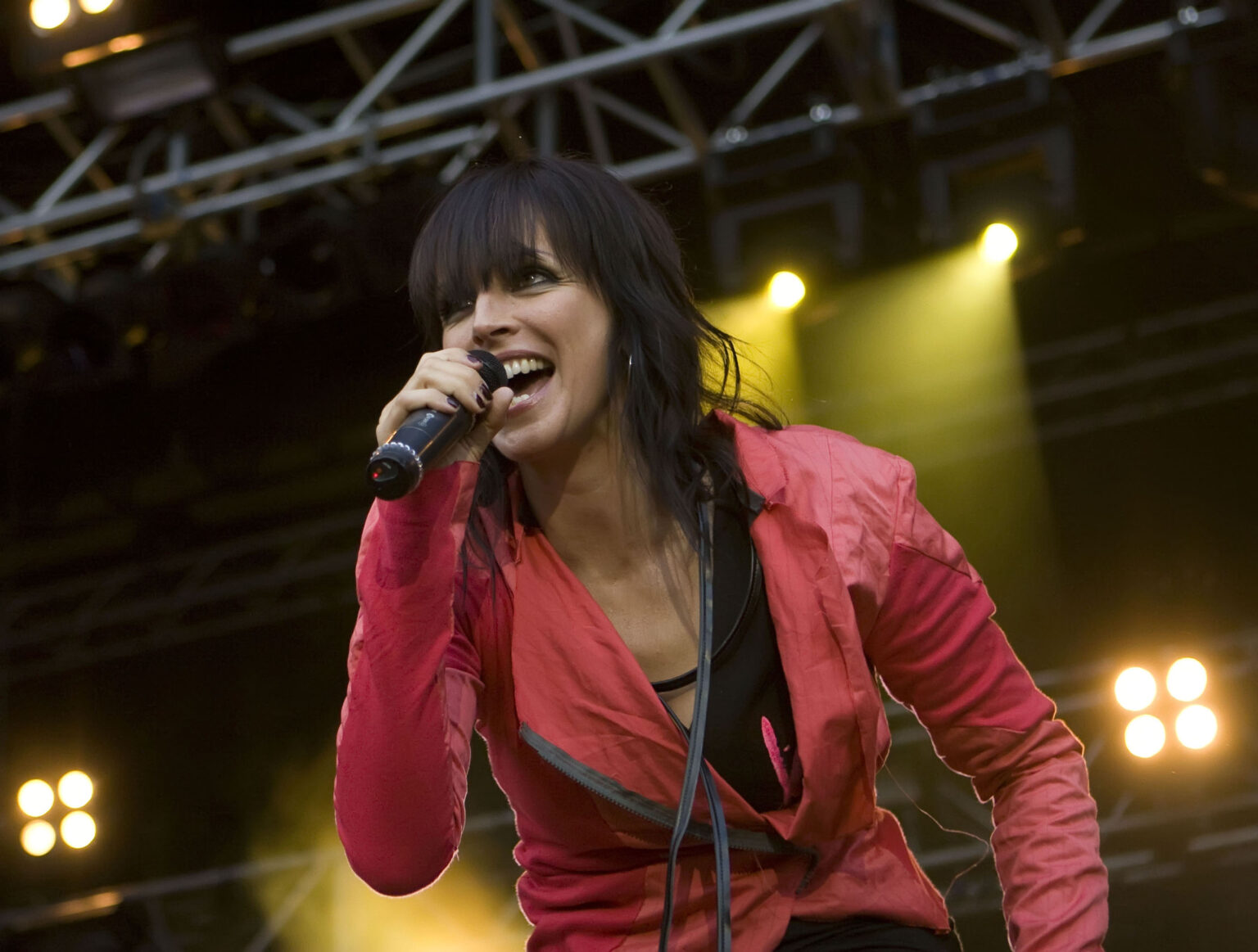Nena mit einer roten Jacke hat ein Mikrofon in der Hand und singt auf einer Bühne