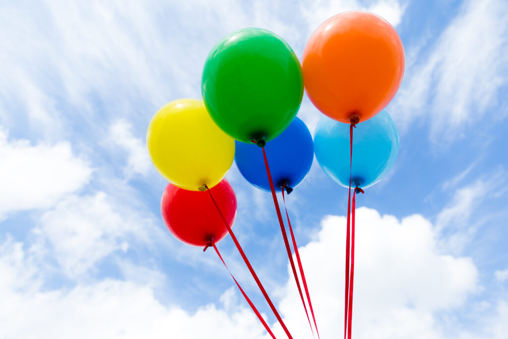 Susanne Kerner Bunte Luftballone an roten Schnüren - dahinter ein blauer Himmel mit Wolken