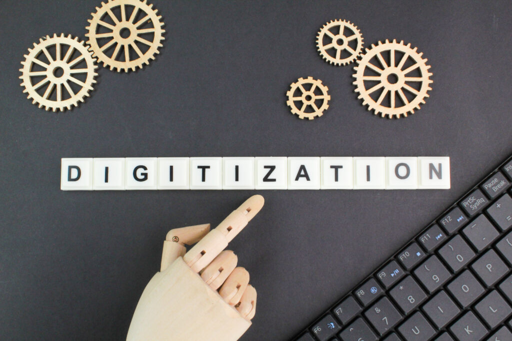 Buchstaben Digitalization dahinter fünf Zahnräder aus Holz, eine Hand aus Holz und ein Anriss einer Tastatur