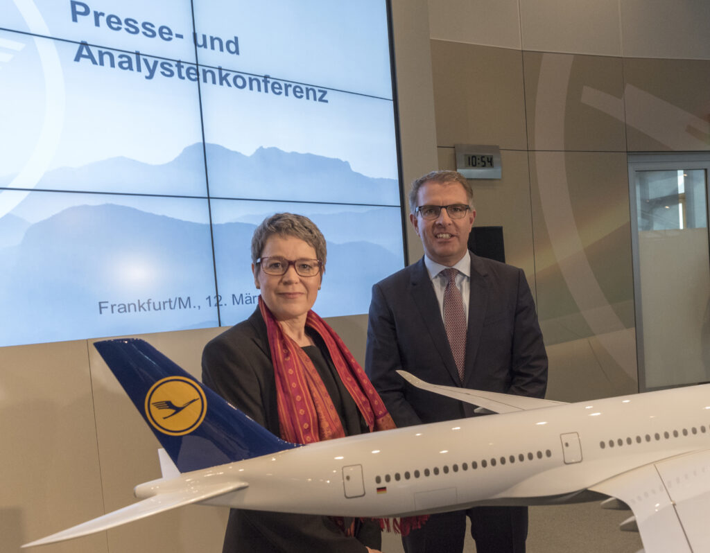 Susanne Menne Susanne Menne steht neben einem Herrn in Anzug. Vor ihnen ein Flugzeug der Lufthansa