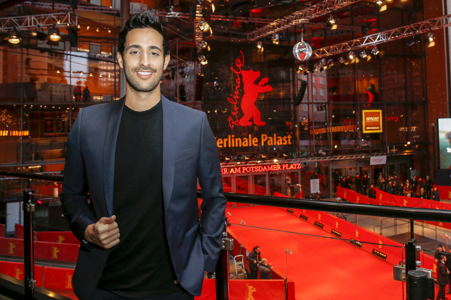 Sami Slimani mit Anzug und schwarzem T-Shirt steht neben einem roten Teppich