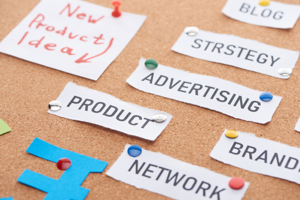 Pinnwand mit aufgepinnten kleinen Papieren auf denen Strstegy, Advertisin, Product, Brand und Network steht