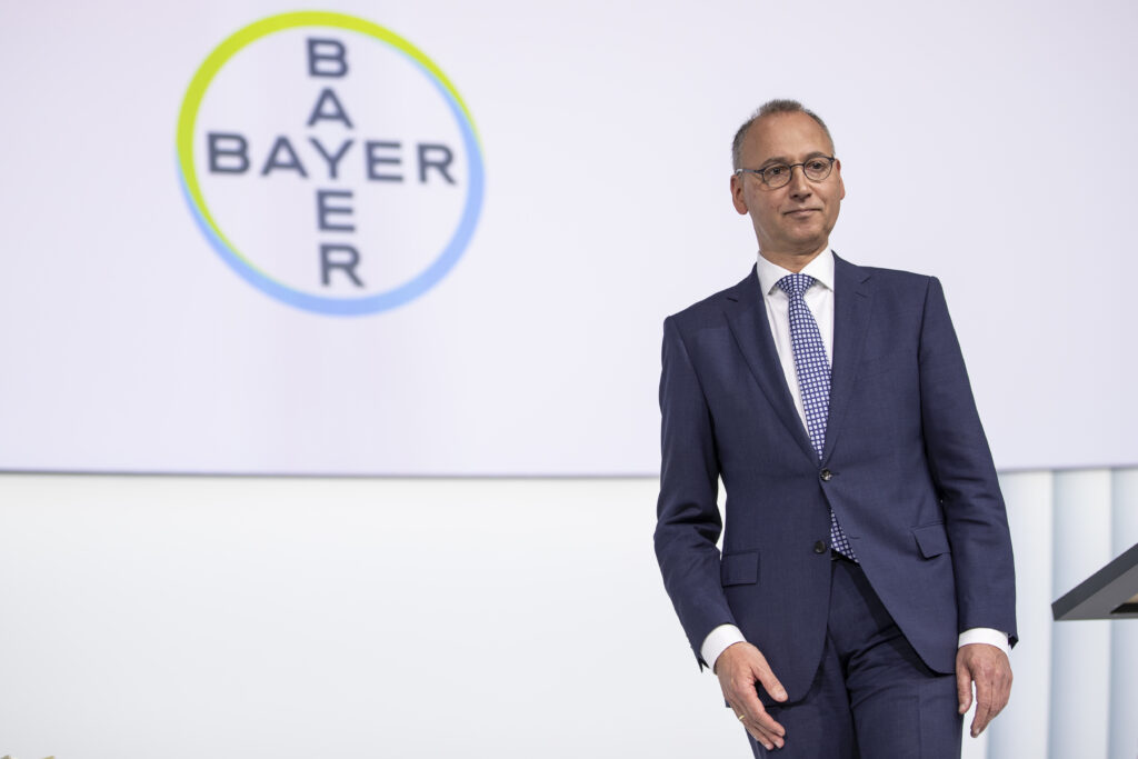 Werner Baumann steht im Anzug vor Bayer-Logo
