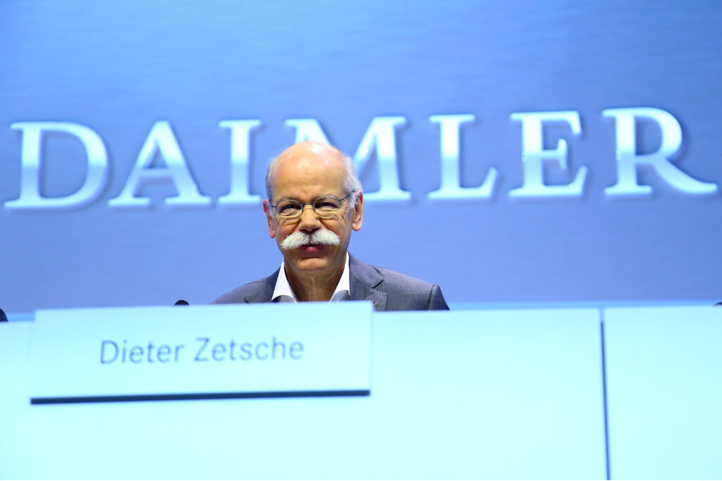 Dieter Zetsche auf einem Podium. Hinter im steht DAIMLER auf einer blauen Wand. Vor ihm sein Namensschild