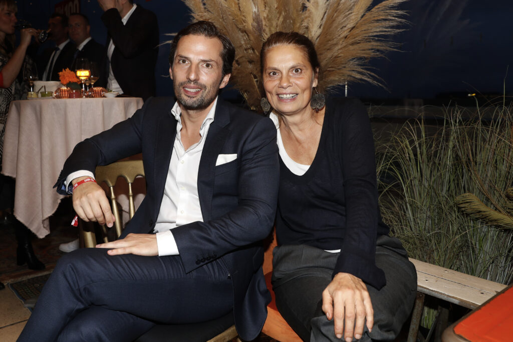 Sarah Wiener Sarah Wiener sitzt neben einem Mann im Anzug und lächelt in die Kamera