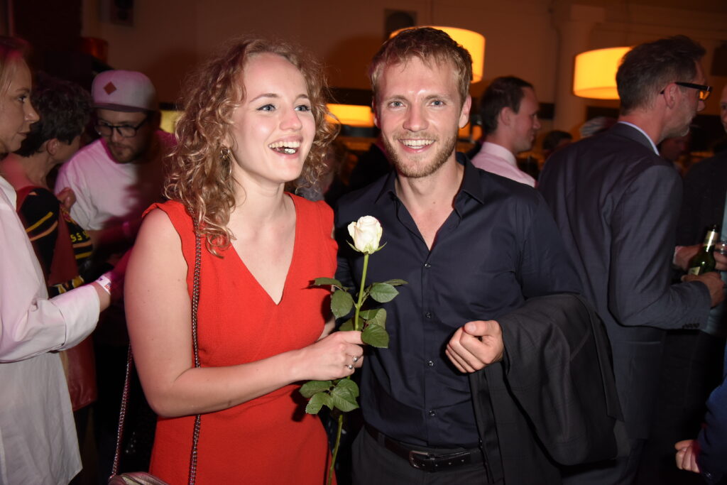 Niklas Osterloh steht neben einer Frau mit rotem Kleid die eine weiße Rose hält