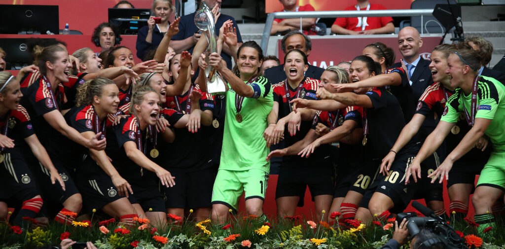 Nadine Angerer mit grünem Dress hält einen Pokal und steht im Kreis mit ihren Kolleginnen