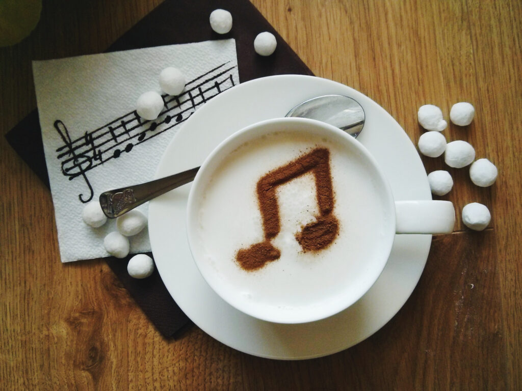 Kaffeetasse mit einer Note aus Kakao im Schaum. Dahinter eine Serviette mit Noten und Mushmallows