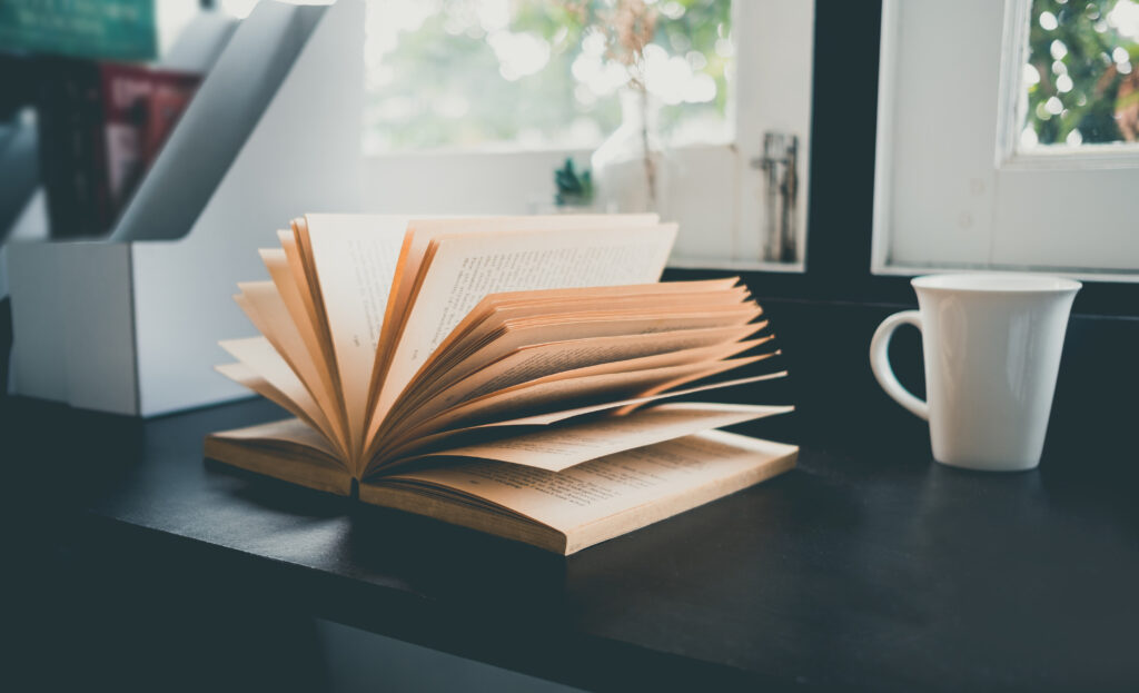 offenes Buch das auf einem schwarzen Tisch liegt. Daneben eine weiße Kaffeetasse