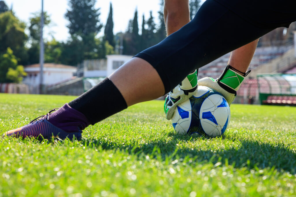 Gestreckter Fuss und zwei Hände die einen Fußball am Boden halten