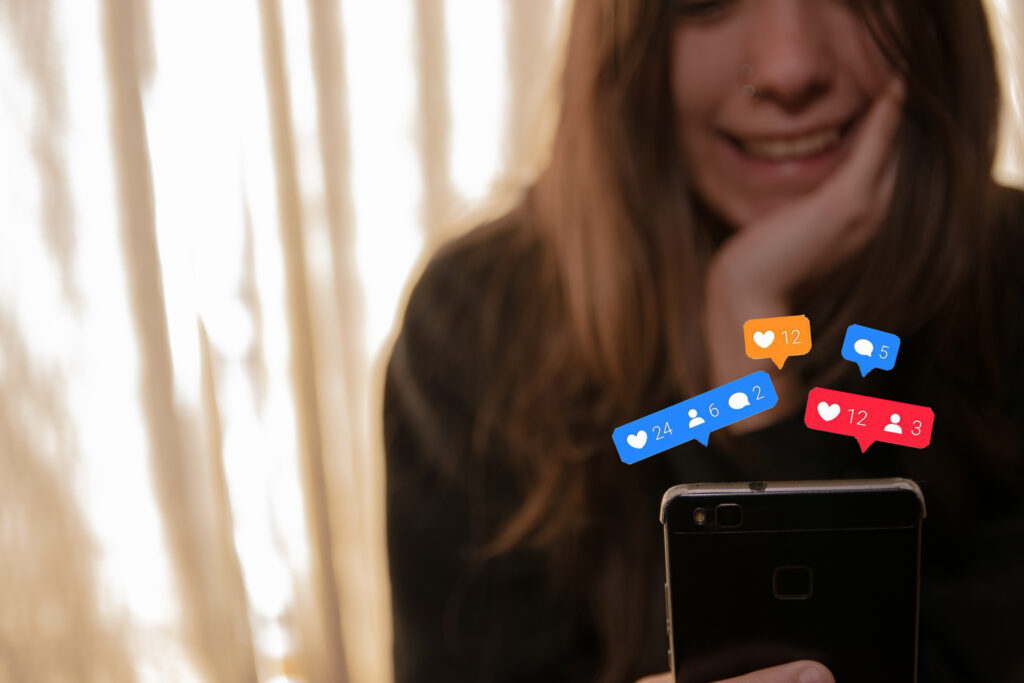 Frau sitzt vor einem Handy; viele Herzen, Sprechblasen und Kommentare