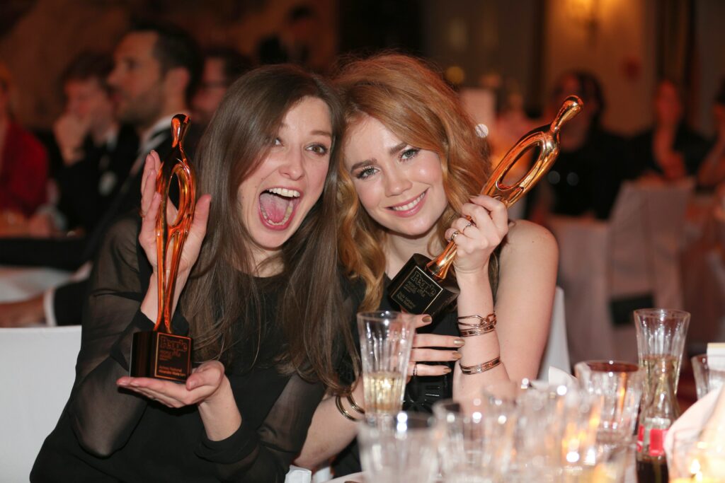 Palina Rojinski mit einer Kollegin lacht in die Kamera und hält eine Trophäe in ihren Händen