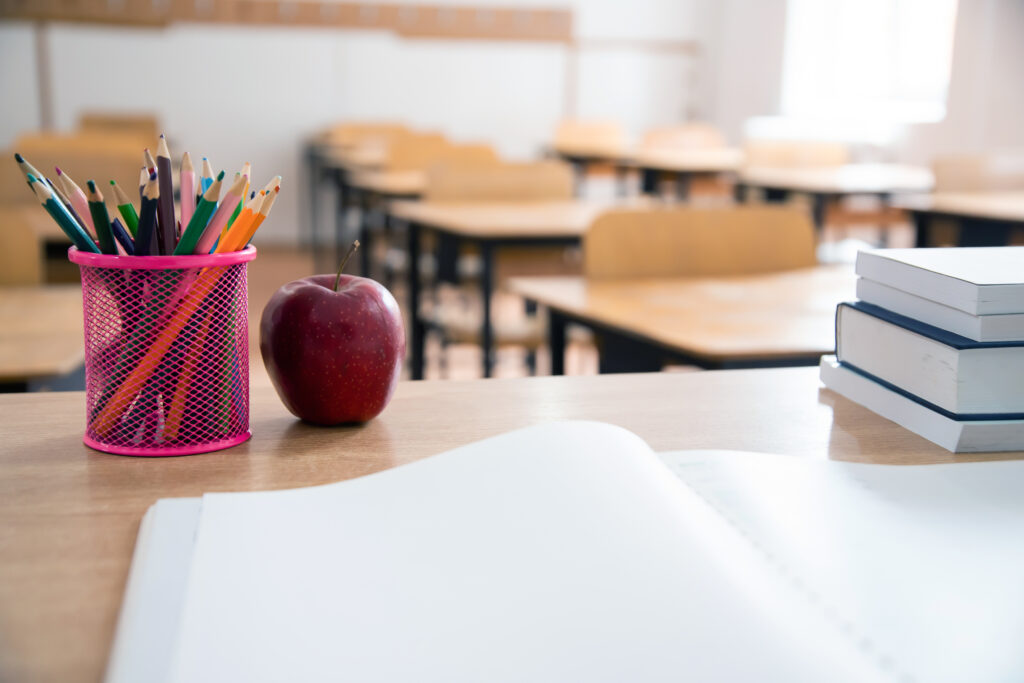 Bleistifte, ein Apfel, Schulbücher und ein aufgeschlagenes Schulbuch