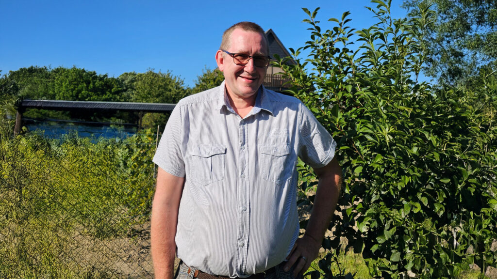 Mann steht in Garten mit Sträuchern im Hintergrund