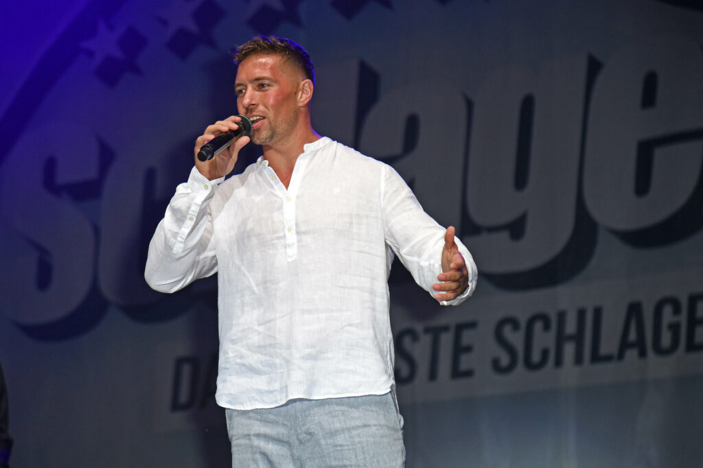 Ramon Roselly mit weißem Hemd und einem Mikrofon in der Hand