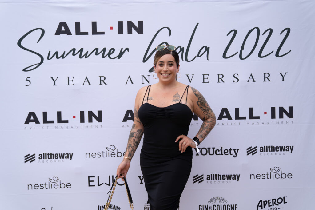 Jolina Mennen steht vor einem Plakat in schwarzem Kleid