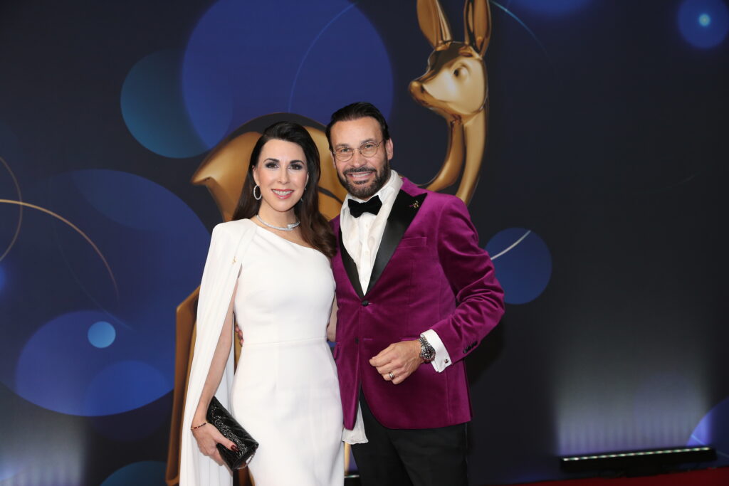 Judith Williams mit weißen Kleid steht neben einem Mann mit violettem Sakko