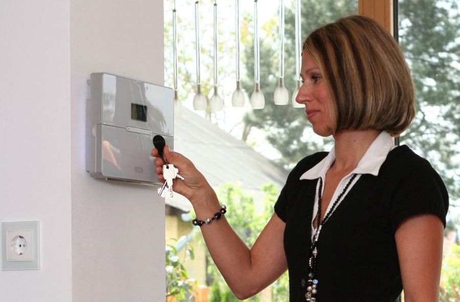 Eine Indoor-Szene mit einer Person, die ein steuerbares Sicherheitsgerät bedient. Im Hintergrund deutet ein Fenster mit begrünter Aussicht auf eine harmonische Umgebung hin.